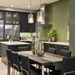 Modern black and sage green kitchen with sleek flat-panel cabinets, stainless steel appliances, white countertops, and a matching dining table with black chairs. Two glass pendant lights hang above, while greenery and tall glass vases soften the clean contemporary design. Faint “Kitchen Informant” watermark at bottom left.