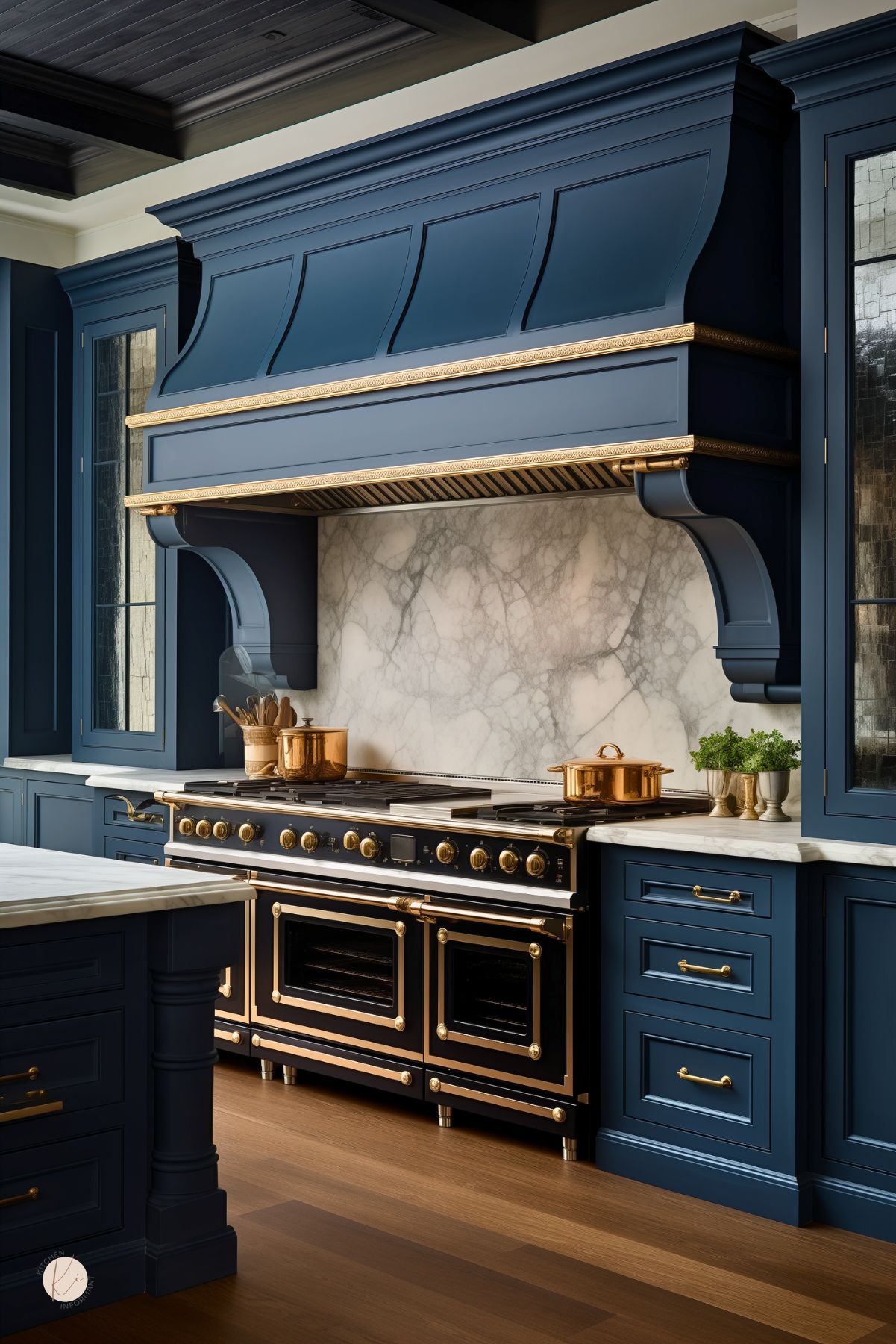 Dark blue luxury kitchen with navy blue cabinets, a dramatic oversized range hood, and a marble backsplash. A large black and brass range with copper pots sits below, paired with brass hardware, white countertops, and warm wood floors. Dark wood ceiling panels and glass-front cabinets add to the upscale kitchen design.