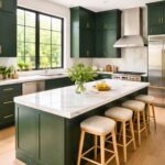 A spacious kitchen with deep green cabinets, white marble countertops, and stainless steel appliances illuminated by natural light.