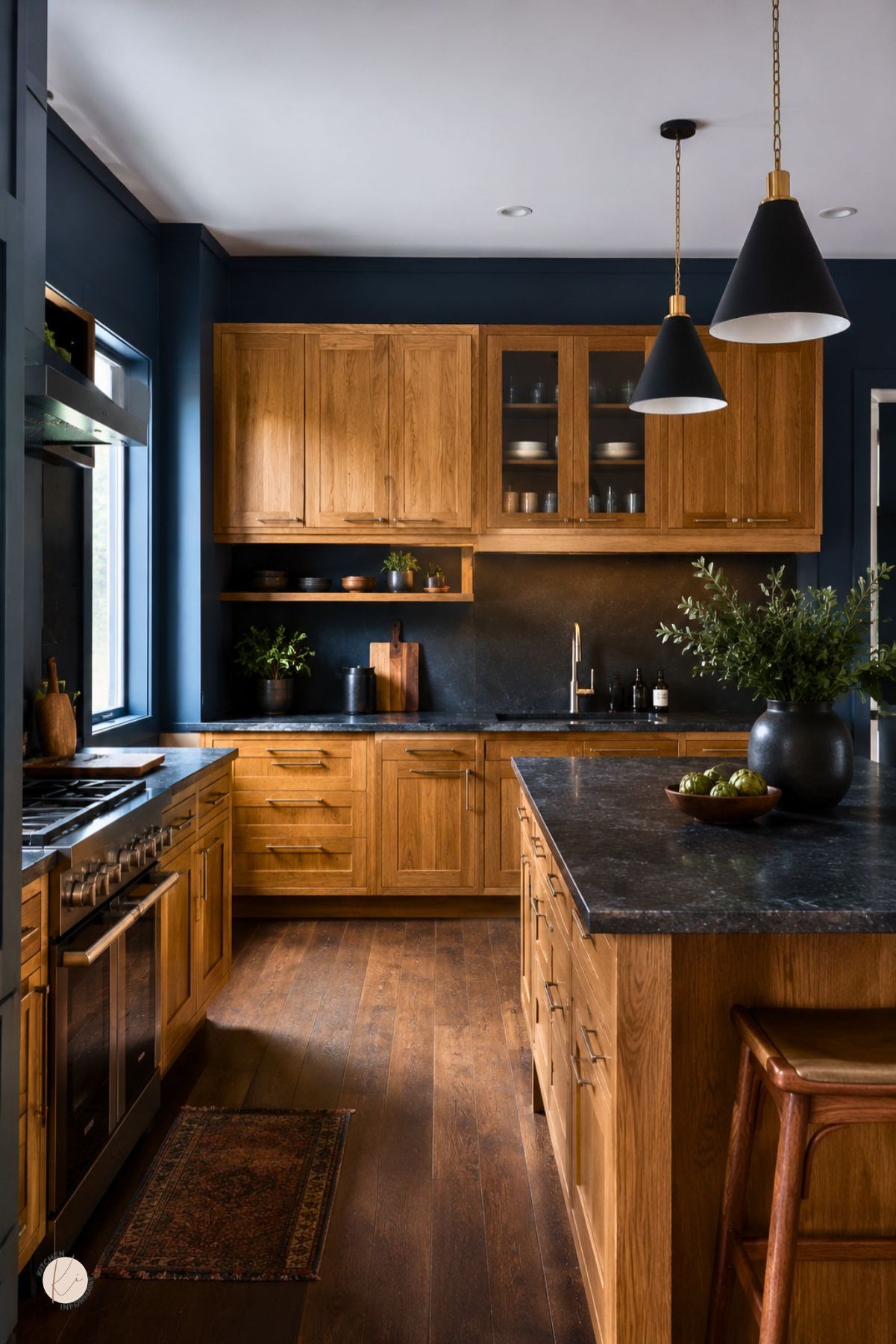 Moody blue kitchen with oak cabinets, black stone countertops, a large island, black pendant lights, stainless range, dark backsplash, wood flooring, patterned runner rug, and warm natural wood accents.