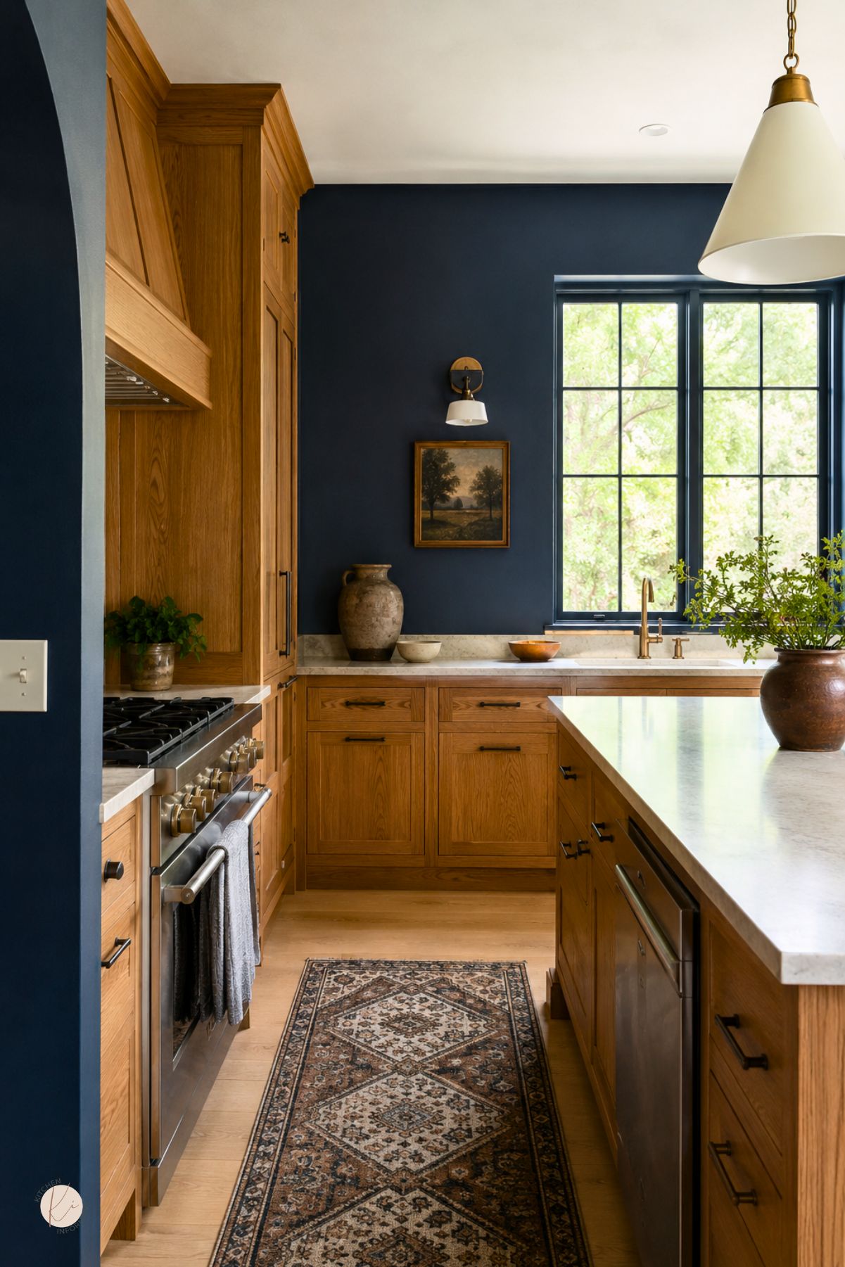 Moody blue kitchen with oak cabinets, white countertops, black hardware, a large island, brass faucet, stainless range, patterned runner rug, wood flooring, and black-framed windows.
