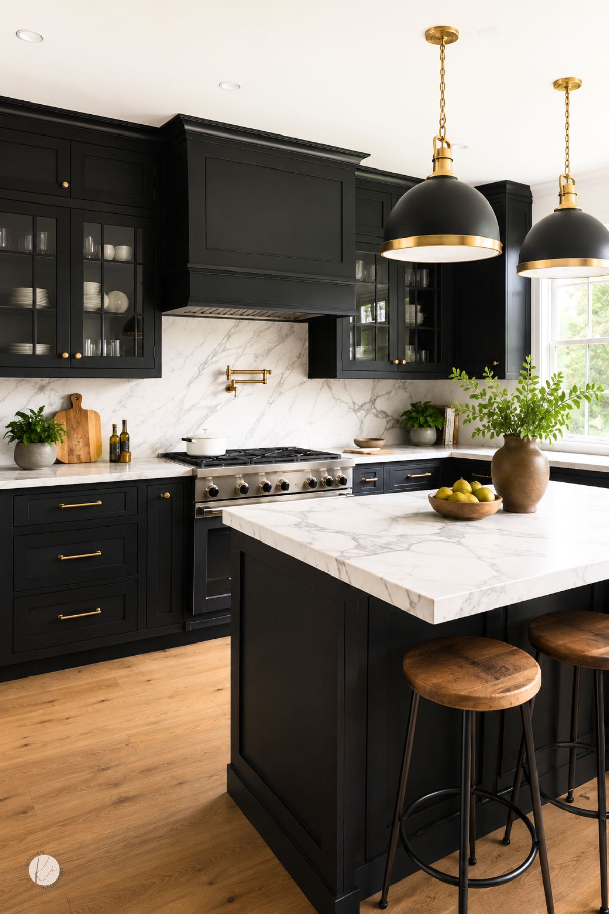 Black kitchen cabinets with brass hardware, marble countertops and matching marble backsplash. A large marble island with wood stools sits under black and gold pendant lights, with glass cabinet doors, a range hood, wood floors, and greenery by a bright window. Text: “Kitchen Informant.”