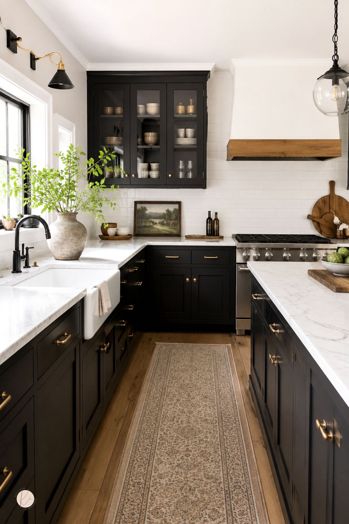 Modern farmhouse kitchen with black cabinets, brass hardware, white marble countertops, and a white subway tile backsplash. A farmhouse sink, glass-front cabinet, wood range hood, black faucet, patterned runner rug, and marble island add warm kitchen design style.