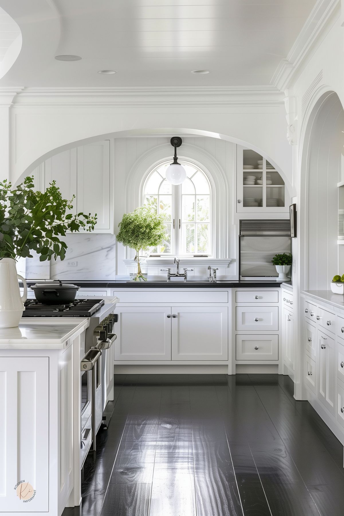 Bright white kitchen with arched architecture, shaker cabinets, black countertops, marble backsplash, glossy dark wood floors, arched window, glass-front cabinet, stainless range, white range hood, chrome faucet, and green plants in natural light.