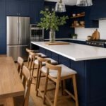 A modern kitchen with navy blue cabinets, white countertops, and oak wood elements like a table or flooring.