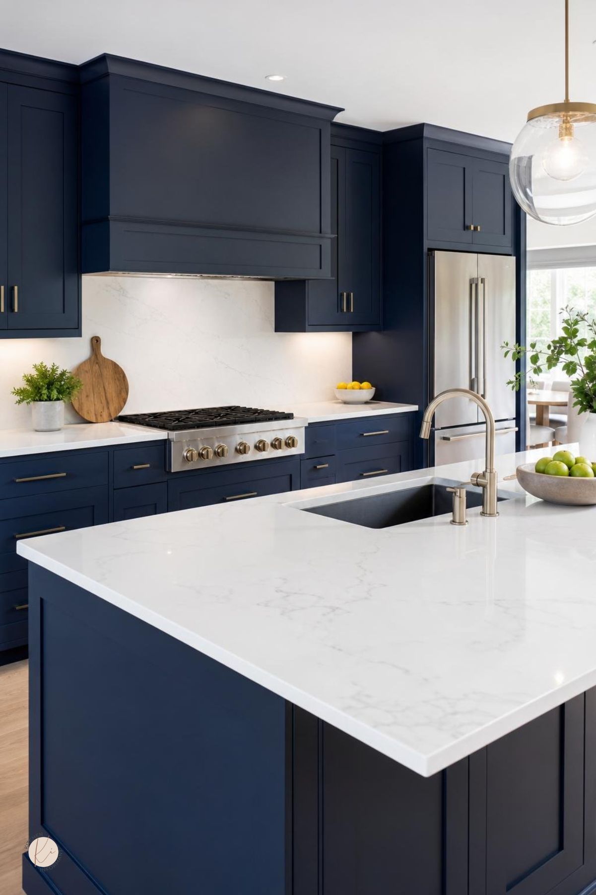 A modern kitchen with navy blue cabinets and white countertops, featuring a built-in sink and stainless steel appliances.