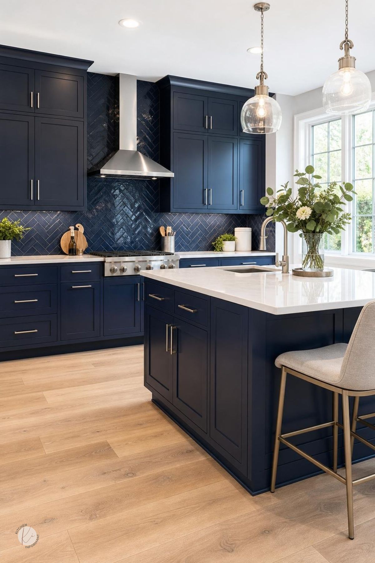 A modern kitchen with navy blue cabinets, white countertops, tiled backsplash, brushed nickel hardware, and light hardwood flooring.