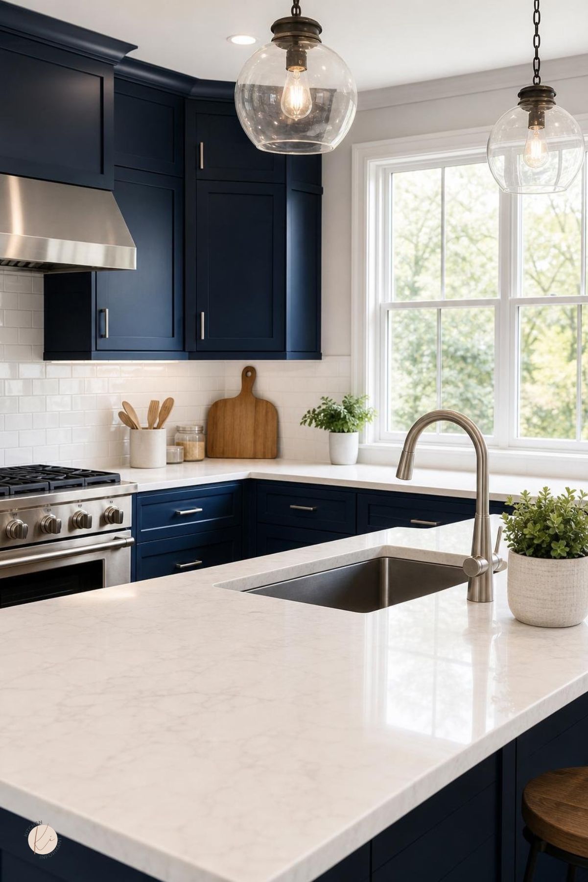 A modern kitchen with navy blue cabinets and white countertops, featuring stainless steel appliances and natural light.